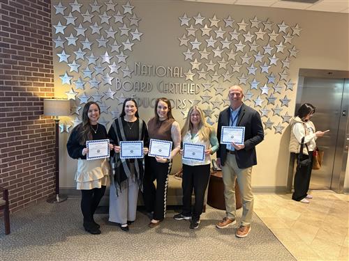 5 of the 11 teachers who renewed their NBCT  in front of the "honor wall" of stars.